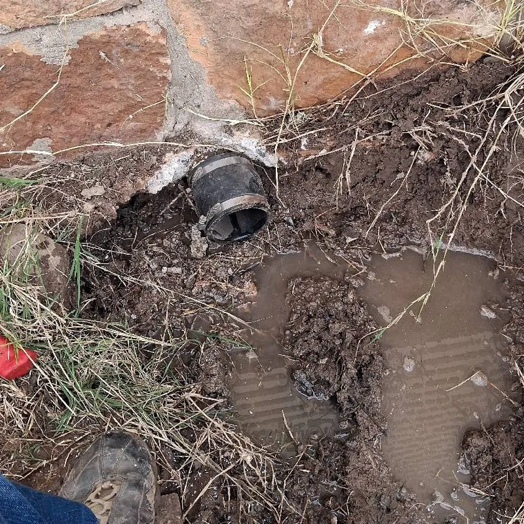 Sewer line connection exposed near a foundation during sewer repair in Warner